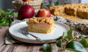 Ein Stück saftiger Apfelkuchen mit Streuseln, perfekt für ein Apfelringe Rezept. Daneben liegen frische Äpfel.