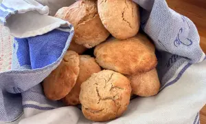 En hög med gyllene, luftiga scones som vilar i en blåvitrandig kökshandduk. Perfekt för fikat!
