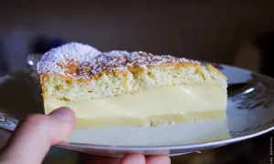 Une part de gâteau magique vanille, saupoudrée de sucre glace, repose sur une assiette. La crème onctueuse contraste avec la texture aérienne du biscuit.
