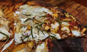 En närbild av en utsökt pizza med kyckling, ost och rosmarin. En smak av pizzans ursprung.