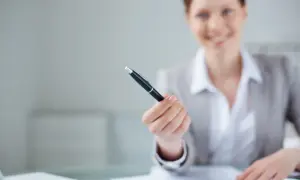 Uśmiechnięty przedsiębiorca oferuje długopis do podpisania ważnej umowy.