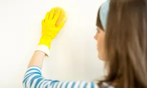 Dłoń w żółtej rękawiczce czyści białą ścianę gąbką.
