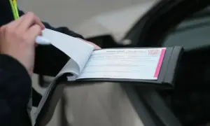 Policjant wypisuje mandat karny w notesie przy samochodzie.