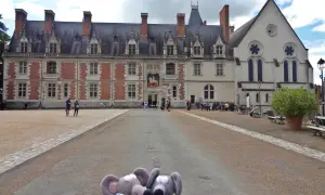 Deux souris en peluche devant le majestueux **château de Blois**. Des visiteurs explorent la cour de ce monument historique.