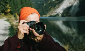 Osoba w pomarańczowej czapce robi zdjęcie aparatem, który mógłby być Nikon D7000. Dane techniczne tego modelu pozwalają na uchwycenie piękna górskiego krajobrazu.