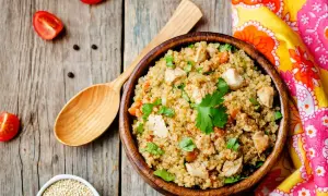 Una ciotola di quinoa con pollo e verdure, un piatto ricco di quinoa valori nutrizionali, su un tavolo di legno con pomodorini e un cucchiaio.