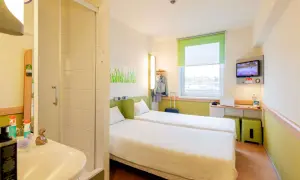 Pokój w hotelu Ibis z dwoma łóżkami, łazienką, biurkiem z laptopem i telewizorem.