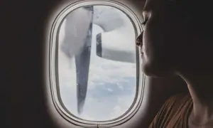 Frau blickt aus dem Flugzeugfenster, während das Flugzeug turbulenzen extrem durchfliegt. Wolken und ein Propeller sind sichtbar.