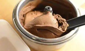Un cucchiaio nero preleva una porzione di cremoso gelato fatto in casa al cioccolato da una gelatiera.