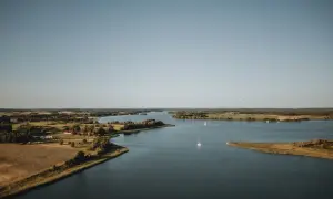 Szerokie jezioro szymoneckie z żaglówkami, otoczone zielonymi polami i lasami. Spokojny dzień na Mazurach.