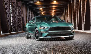En grön pony car, en Ford Mustang, står på ett gallergolv under en bro med belysning.