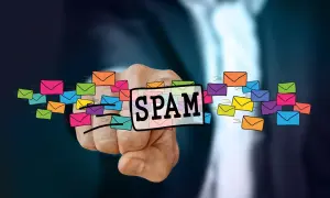 Dłoń wskazuje na napis SPAM otoczony kolorowymi kopertami, symbolizującymi niechciane wiadomości. To definicja spamu.