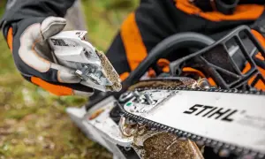 Persona con guantes realiza mantenimiento de motosierra, ajustando piezas cubiertas de serrín.