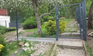 Nowe ogrodzenie z furtką, prawdopodobnie 120 cm wysokości, otacza zielony ogród z kwitnącym drzewem.