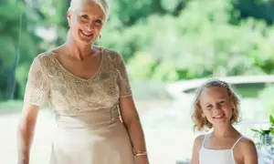 Elegancka stylizacja na komunię dla babci. Uśmiechnięta kobieta w beżowej sukni z haftem i dziewczynka w bieli.