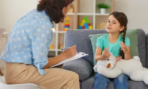 Psychoterapeutka z notatkami rozmawia z dziewczynką trzymającą misia.