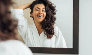 Uśmiechnięta kobieta w szlafroku podziwia swoje naturalne, falowane włosy, prezentując różne typy skrętu.