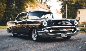 Svart Chevrolet Bel Air bil från 1957 parkerad på grusväg med höstlöv.