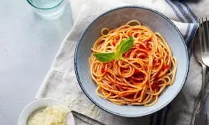 Misternie ułożone spaghetti z sosem pomidorowym i listkiem bazylii. Obok miseczka z tartym parmezanem. Idealne pytanie: jakie przyprawy do spaghetti?