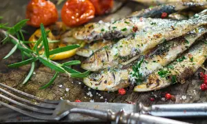 Délicieuses sardines à la plancha, parsemées d'herbes fraîches, accompagnées de tomates cerises rôties et d'une branche de romarin sur fond de bois rustique.