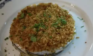 Tortino di alici dorato e croccante, guarnito con prezzemolo fresco, servito su un piatto bianco con bordo blu.