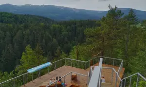 Drewniany punkt widokowy w Karpaczu z widokiem na góry i las. Dwie osoby odpoczywają na platformie.