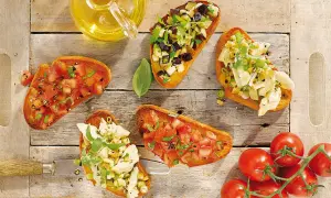 Fünf Bruschetta-Varianten mit Tomaten, Auberginen und Artischocken auf Holzhintergrund.