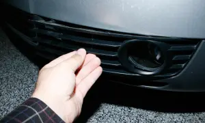 Dłoń naciska na kratkę zderzaka Audi A6 C5, obok otworu na światło przeciwmgielne.