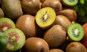 Ein Haufen Kiwis, einige ganz, andere aufgeschnitten, zeigen ihr grünes und gelbes Fruchtfleisch. Perfekt für einen gesunden Snack vor dem Schlafen.