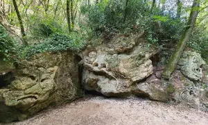 Volto scolpito nella roccia lungo il sentiero Li Vurgacci, circondato da vegetazione lussureggiante.