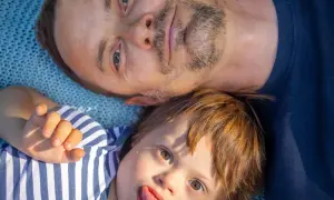 Un padre e il suo bambino con sindrome di Down, un neonato con un'espressione giocosa, sdraiati su una coperta blu.
