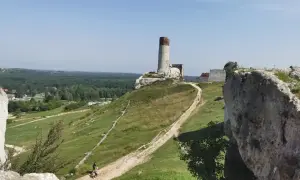 Ruiny zamku na wzgórzu, z wieżą i fragmentami murów. W dole ścieżka, idealna na rowerowe wycieczki po okolicach Częstochowy.