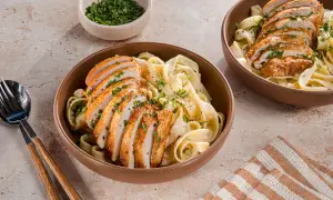 Zwei Schüsseln cremiger Pasta mit geschnittenem Hähnchenbrustfilet, bestreut mit Petersilie. Ein köstliches Chicken Alfredo Rezept für jeden Anlass.