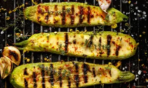 Drei perfekt gegrillte Zucchinischiffchen mit Kräutern und Gewürzen auf einem Grillrost. Ein Genuss für Augen und Gaumen!