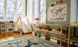 A child's playroom set up with the Montessori method at home, featuring a tent, world map, and wooden shelves with educational toys and books.