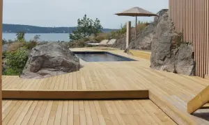 En stor altan i trä med pool och solstolar, omgiven av klippor och med utsikt över havet. Trall mått är perfekt för detta sommarparadis.