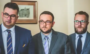 Trzech mężczyzn w garniturach i okularach, stojących obok siebie.