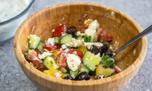 En fräsch sallad till pajen med tomat, gurka, fetaost och oliver i en träskål.
