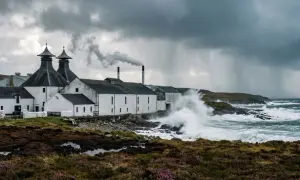 Distillerie sur l'île d'Islay, battue par les vagues et la pluie sous un ciel orageux. La fumée s'échappe d'une cheminée.