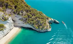 Piękna plaża i turkusowe morze, idealne miejsce, by zastanowić się, gdzie do Włoch na wakacje. Statek wycieczkowy zbliża się do skalistego wybrzeża.