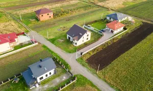 Domy na wsi, zróżnicowana odległość domu od plotu, otoczone polami i zielenią.