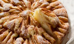 Una deliziosa torta di mele, cosparsa di zucchero a velo, con una fetta appena tolta che rivela la morbidezza dell'impasto e le mele caramellate.