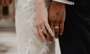 Manos entrelazadas, luciendo los anillos de casado. Ella, con un vestido de encaje, él, con traje oscuro.