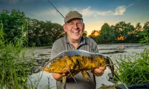 Glücklicher Angler hält großen Fisch am Lohheider See im Abendlicht.