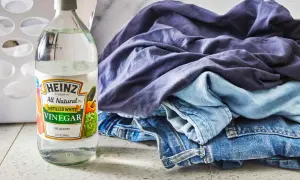 Butelka octu do prania Heinz obok sterty niebieskich ubrań i dżinsów.