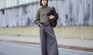 Stylisches Outfit: Eine Frau kombiniert eine graue Hose mit einem gemusterten Strickpullover und einer voluminösen Tasche.