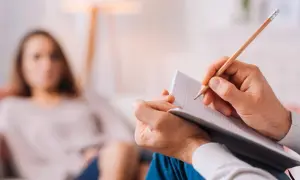 Un terapeuta annota pensieri durante una seduta di terapia psicologica breve. Una donna sfocata ascolta attentamente.