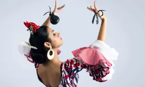 Bailarina flamenca con castañuelas y peinados sevillana, luciendo un vestido de lunares y volantes.