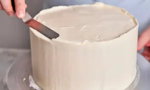 Eine Hand glättet mit einem Spatel die cremige Buttercreme-Torte.