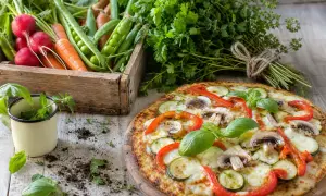 Délicieuse pizza chou fleur garnie de légumes frais, avec une caisse de radis, carottes et petits pois en arrière-plan.